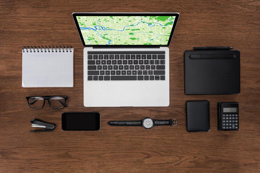 Ansicht des Arbeitsplatzes mit leerem Lehrbuch, Smartphone, Armbanduhr und Laptop mit Karte auf dem Bildschirm - Foto, Bild