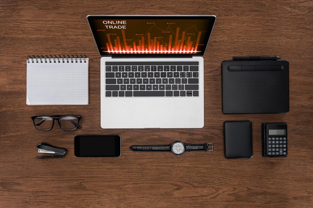 Ansicht des Arbeitsplatzes mit geordnetem leeren Lehrbuch, Smartphone, Armbanduhr und Laptop mit Online-Handel auf dem Bildschirm - Foto, Bild