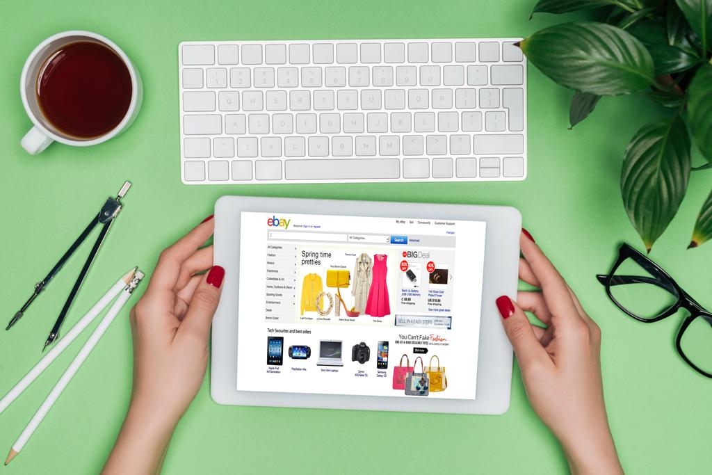 Oříznout obrázek ženské architekta drží digitální tablet s ebay na obrazovce u stolu s rozdělovačem, kávy a v květináči  - Fotografie, Obrázek