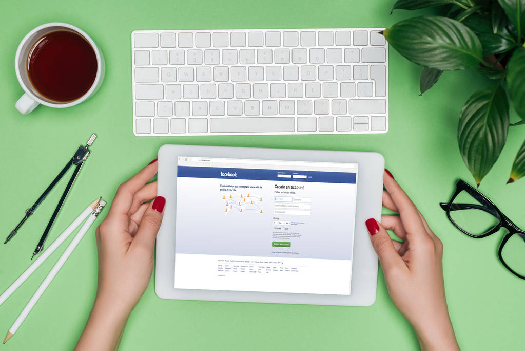Oříznout obrázek ženské architekta drží digitální tablet s facebook na obrazovce u stolu s rozdělovačem, kávy a v květináči  - Fotografie, Obrázek