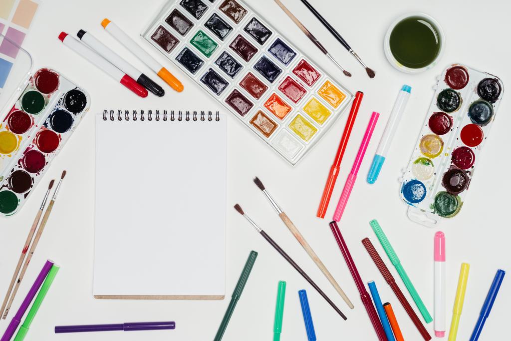 Draufsicht auf den Künstler-Arbeitsplatz mit leerem Lehrbuch, Pinseln, bunten Farben und Filzstiften  - Foto, Bild