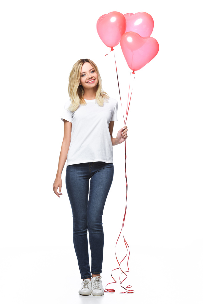 schönes Mädchen in lässiger Kleidung hält Bündel von herzförmigen Luftballons isoliert auf weiß - Foto, Bild