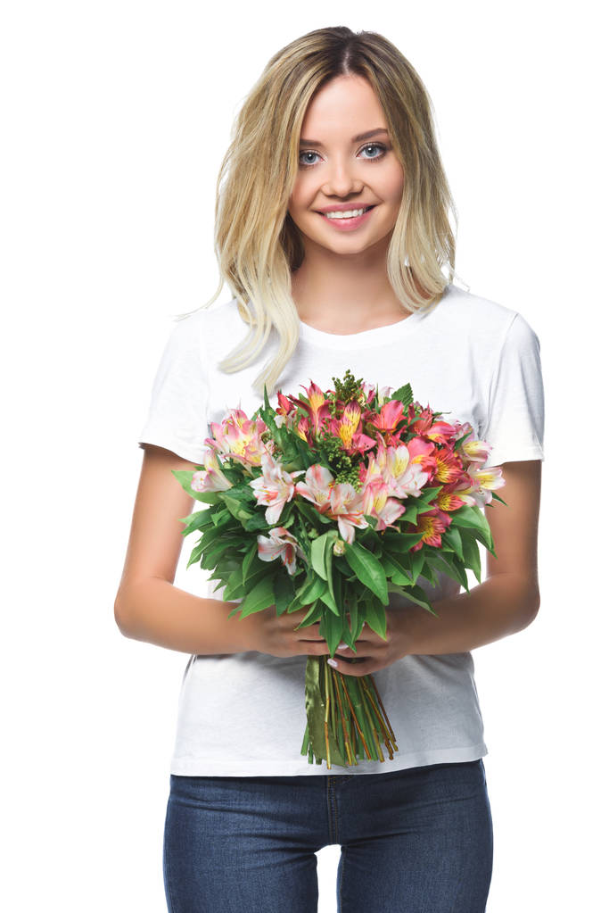 usmívající se atraktivní dívka drží kytici květin a při pohledu na fotoaparát izolované na bílém - Fotografie, Obrázek