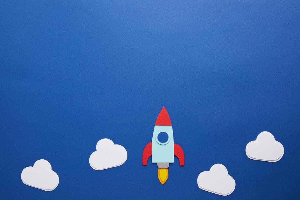 clouds and rocket on blue paper background with copy space - Photo, Image