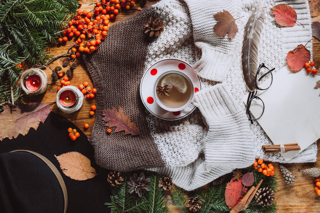 Stylish Flat lay view of autumn leaves and tartan textured sweater on wooden background with cup of tea. Концепция осени или зимы
.  - Фото, изображение