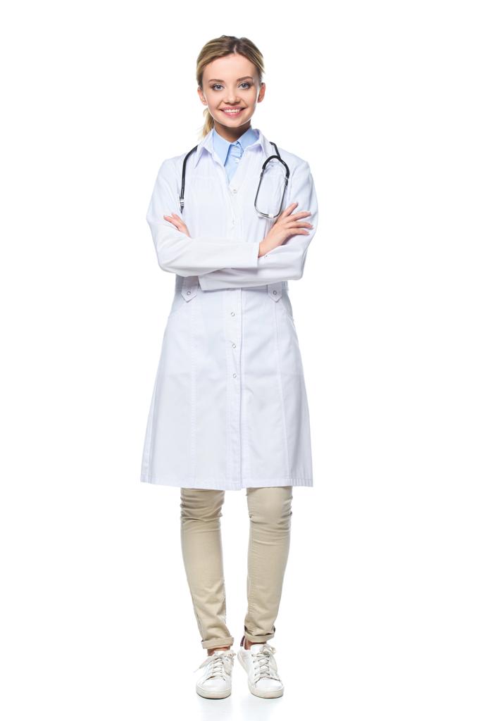 junge Ärztin im weißen Mantel posiert mit verschränkten Armen, isoliert auf weiß - Foto, Bild