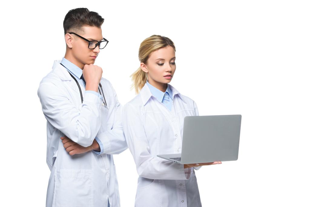Młodzi lekarze zamyślony w białych płaszczach za pomocą laptopa, na białym tle - Zdjęcie, obraz