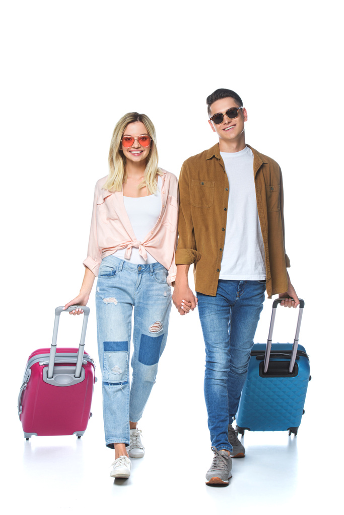 young happy couple holding hands and walking with suitcases isolated on white - Photo, Image