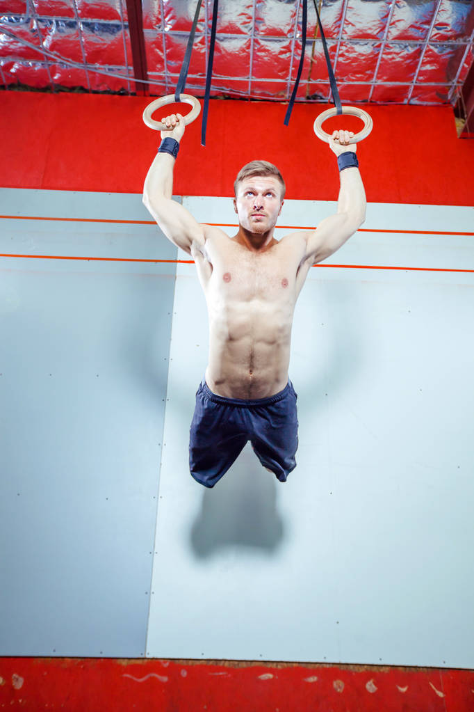 Exercice de musculation jeune homme faisant de l'exercice de cross fit intense à la salle de gym sur des anneaux de gymnastique
. - Photo, image