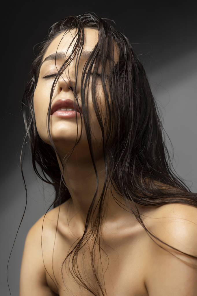 Gyönyörű barna lány divat modell meztelen váll és a nedves haj egy szürke háttér. Meztelen make-up. Egészséges tiszta bőr. Reklám- és kereskedelmi tervez. - Fotó, kép