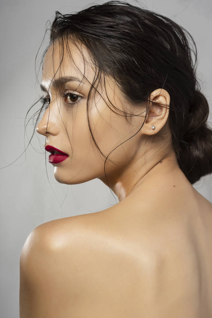 Mooie brunette meisje mannequin met naakte schouders en natte haren op een grijze achtergrond. Naakt make-up, rode lippen. Gezonde schone huid. Reclame en commerciële design. - Foto, afbeelding