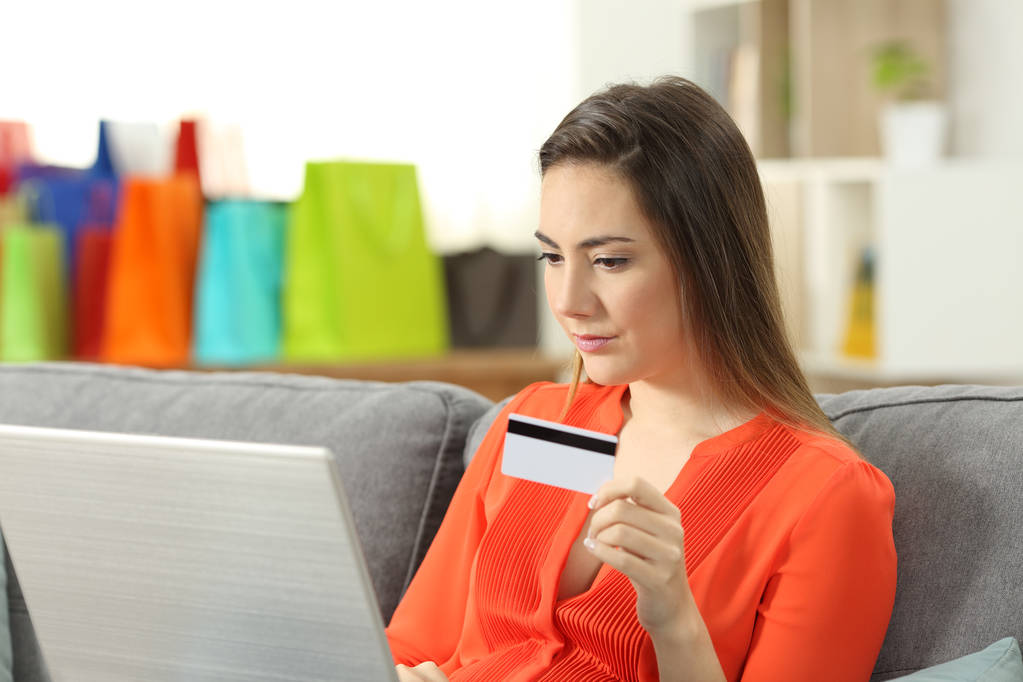 Lady online betalen met een creditcard en een laptop zittend op een bank in de huiskamer - Foto, afbeelding