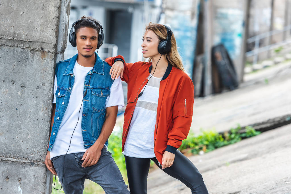 stylowe wielokulturowym para z słuchawki, stojąc przy ulicy miasta  - Zdjęcie, obraz