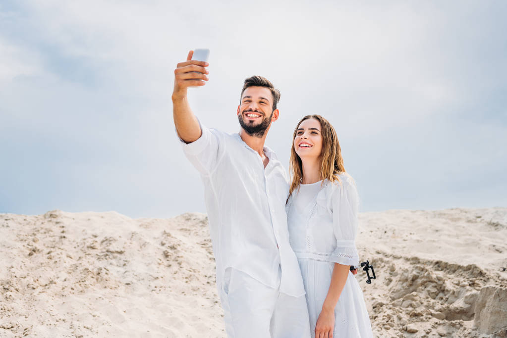 glückliches junges Paar in weißen Kleidern macht Selfie in der Wüste - Foto, Bild