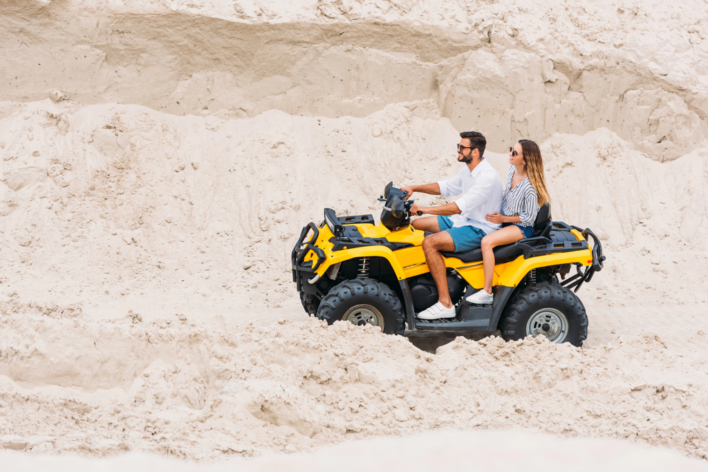χαμογελώντας νεαρό ζευγάρι Καβάλα παντός εδάφους όχημα στην έρημο - Φωτογραφία, εικόνα