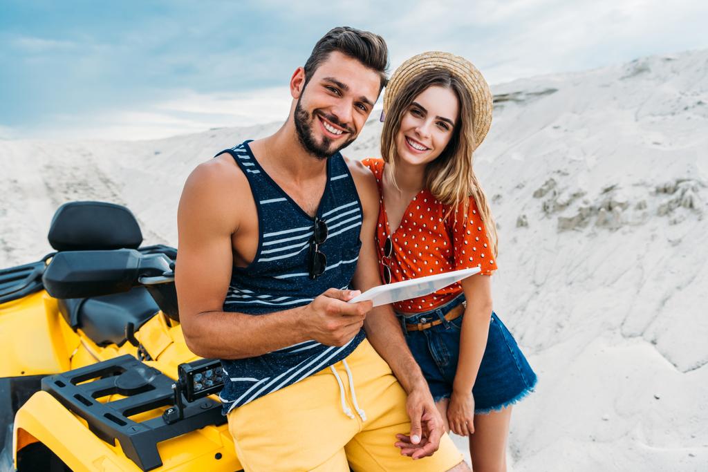 happy young couple with ATV using digital tablet in desert and looking at camera - Photo, Image