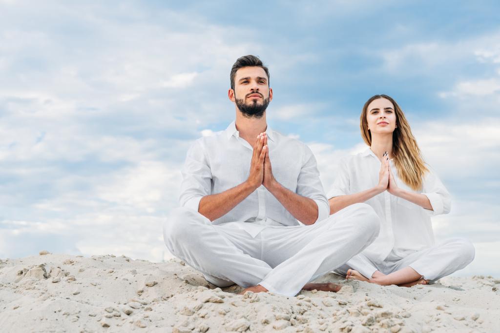 hermosa pareja joven practicando yoga mientras se sienta en una duna de arena en pose de loto (padmasana
) - Foto, imagen