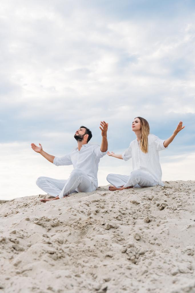 young fit couple on yogi meditating while sitting on sandy dune in lotus pose (padmasana) - Photo, Image