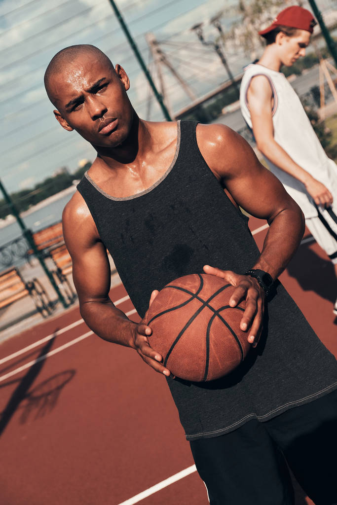 serio joven africano en ropa deportiva mirando a la cámara y sosteniendo la pelota de baloncesto
 - Foto, Imagen
