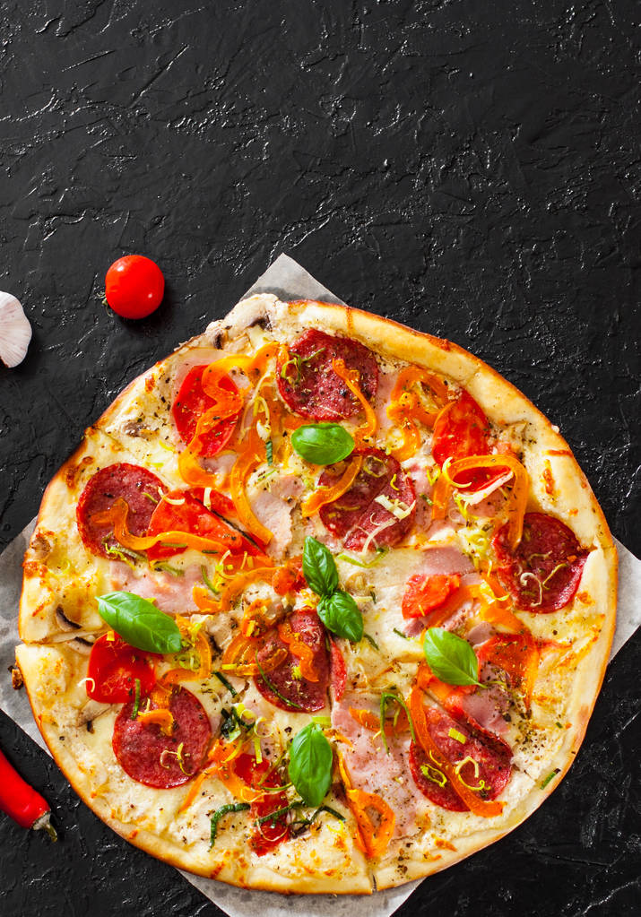 Pizza s Mozzarella sýr, šunka, rajčata, salám, pepř, feferonky koření a čerstvé bazalky. Italské pizza.on černé pozadí. s prostorem kopie. pohled shora - Fotografie, Obrázek