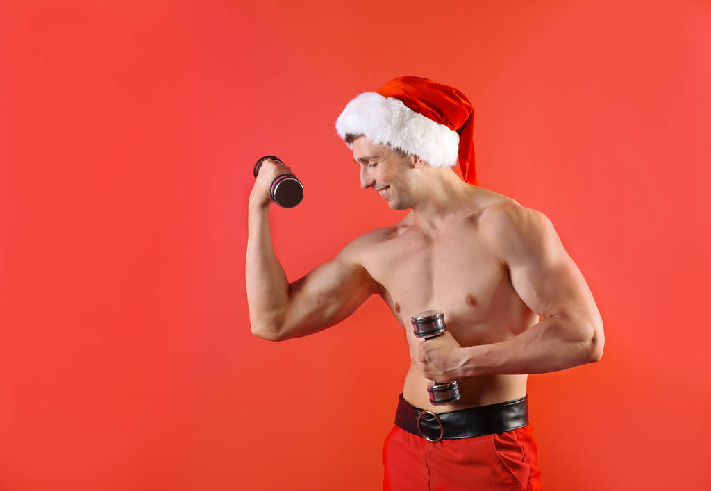 Giovane uomo muscoloso in cappello Babbo Natale con manubri su sfondo colore
 - Foto, immagini