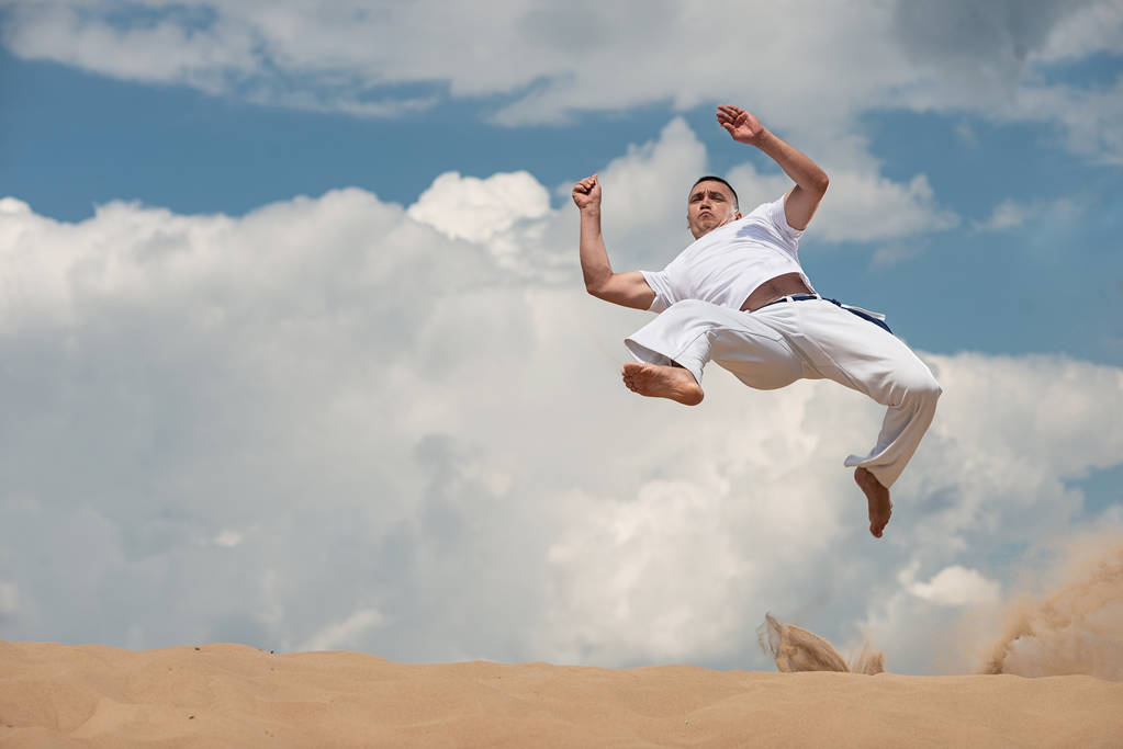 Um jovem treina capoeira contra o céu. O conceito de pessoas, estilo de vida e esportes. Um homem faz um pontapé no salto
 - Foto, Imagem
