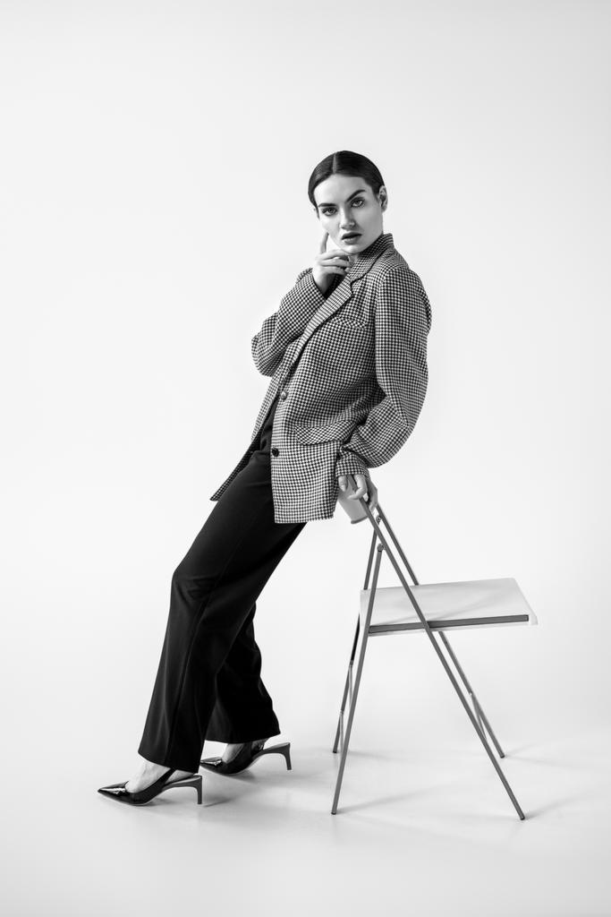 美しいグラマー モデル ポーズ椅子 グレーに近いおしゃれなビンテージ スーツの黒と白 ロイヤリティフリー写真 画像素材