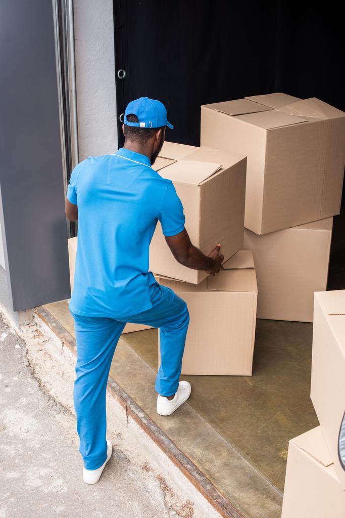 back view of african american delivery man putting boxes on pile - Photo, Image