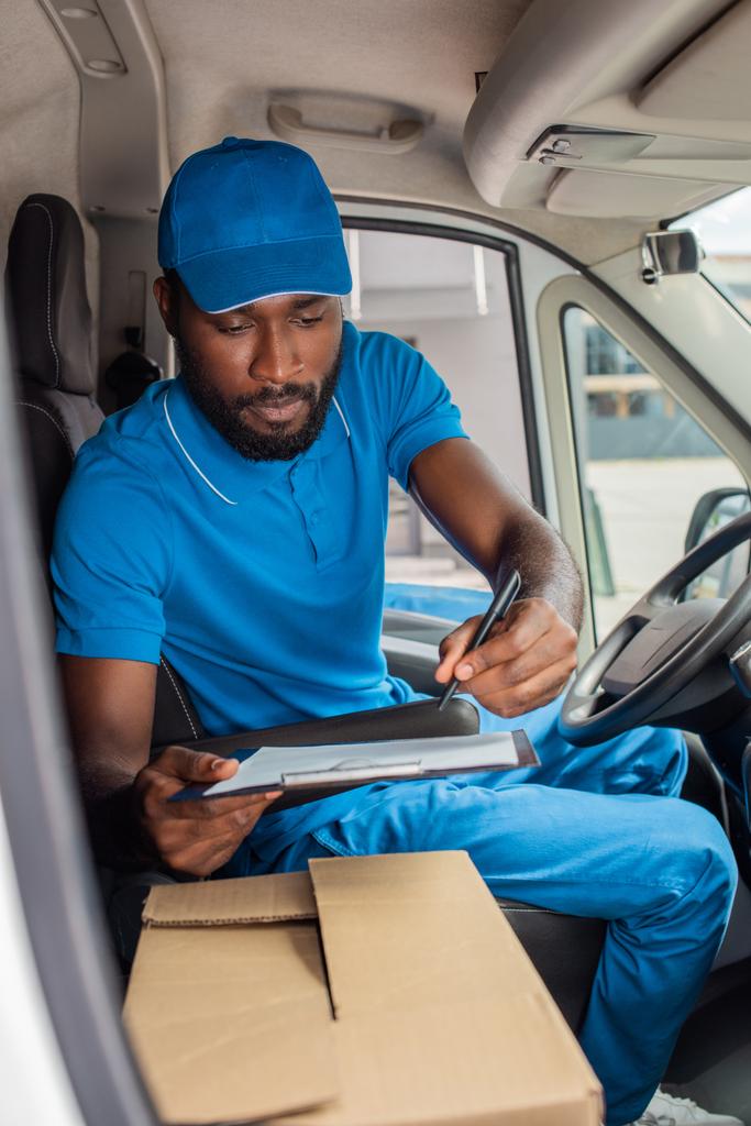 Afrikanisch-amerikanischer Zusteller hält Klemmbrett und Stift in Transporter  - Foto, Bild
