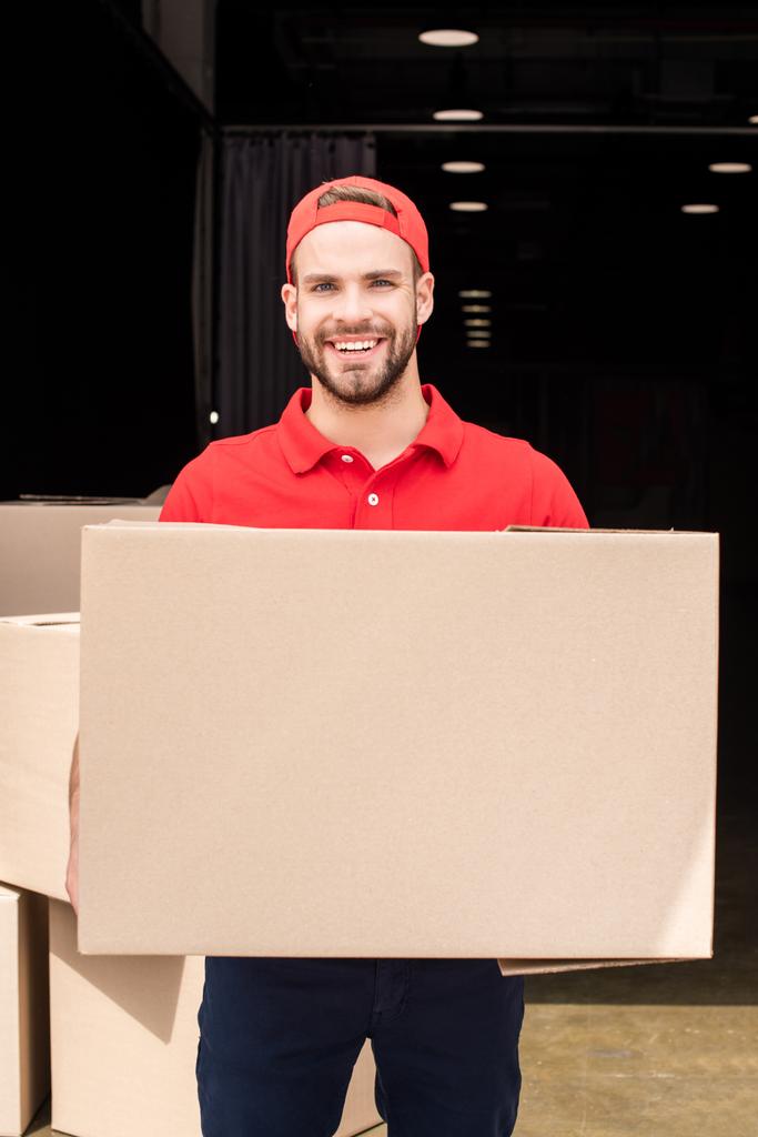 Portret van glimlachen levering man in uniform met kartonnen doos - Foto, afbeelding