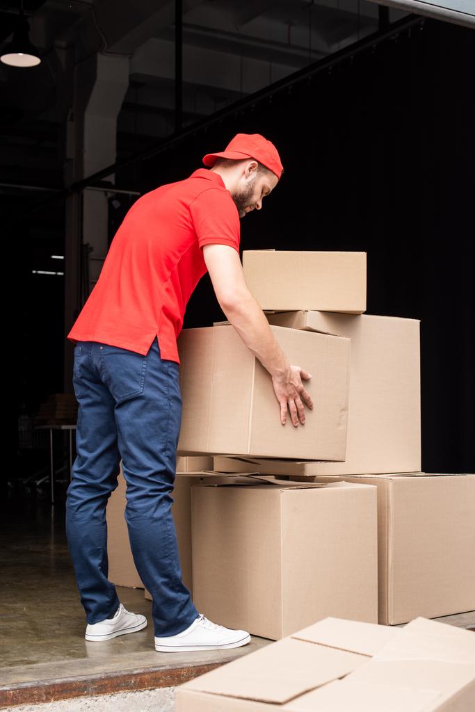 joven repartidor en uniforme rojo con cajas de cartón
 - Foto, Imagen