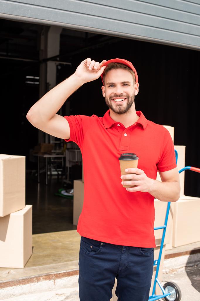 portrait of cheerful delivery man with coffee to go in hand and cargo behind - Photo, Image