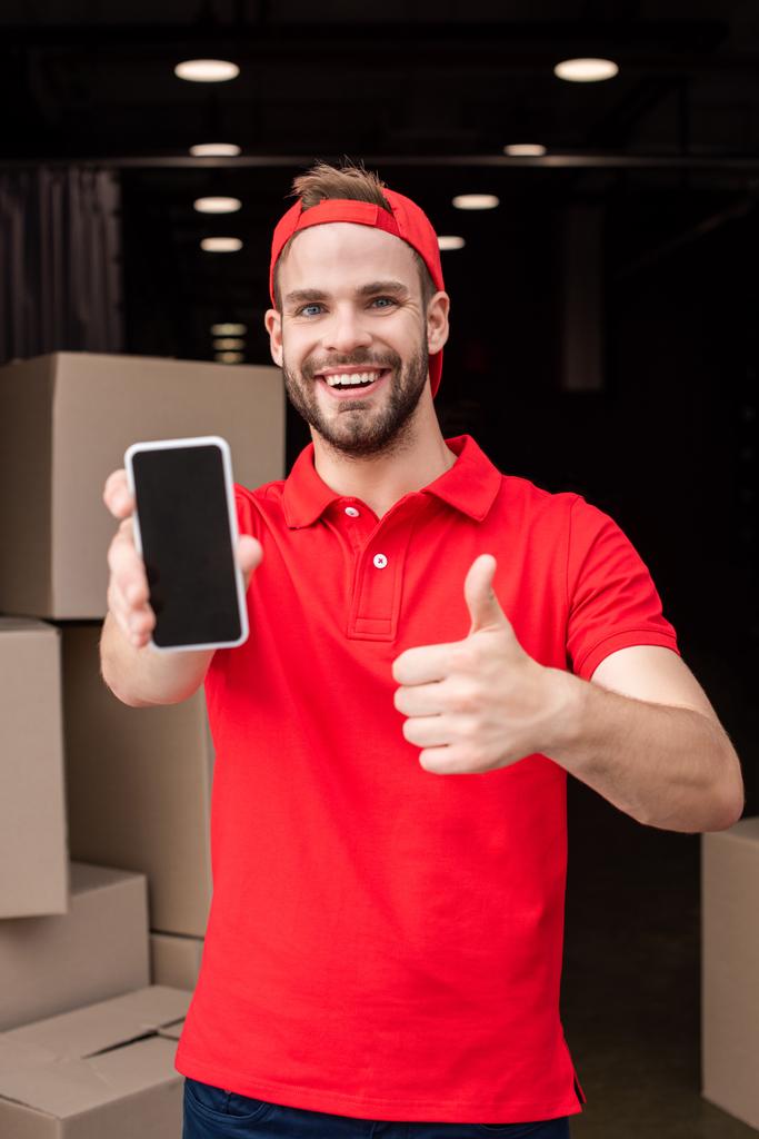 portrait of cheerful delivery man with smartphone showing thumb up - Photo, Image