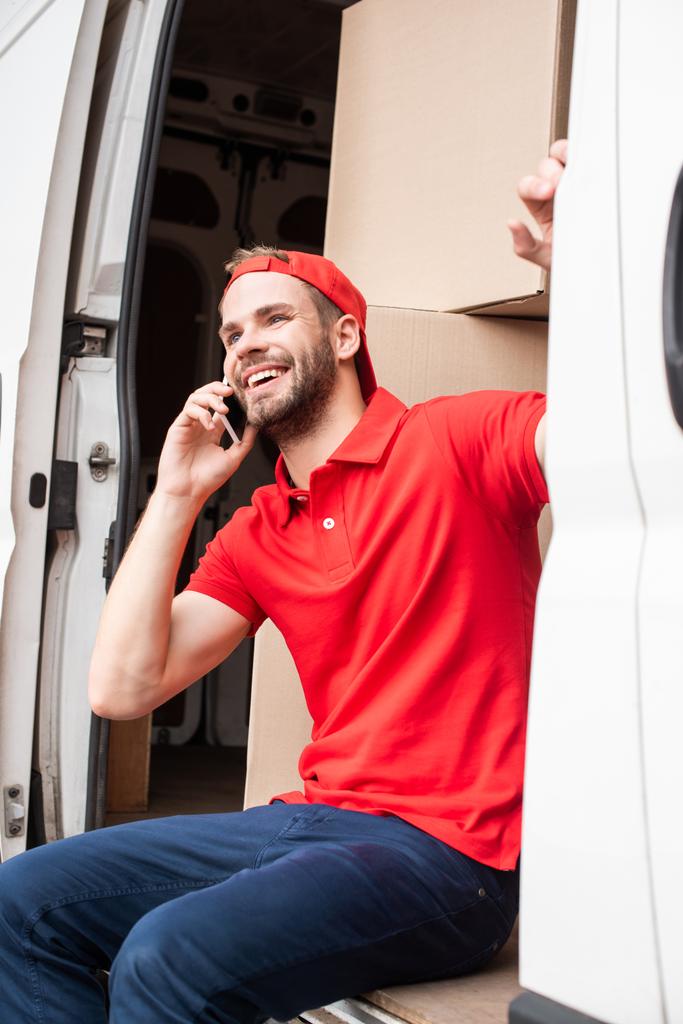 uśmiechnięty człowiek dostawy w czerwony jednolite rozmawia smartfona podczas odpoczynku w van - Zdjęcie, obraz