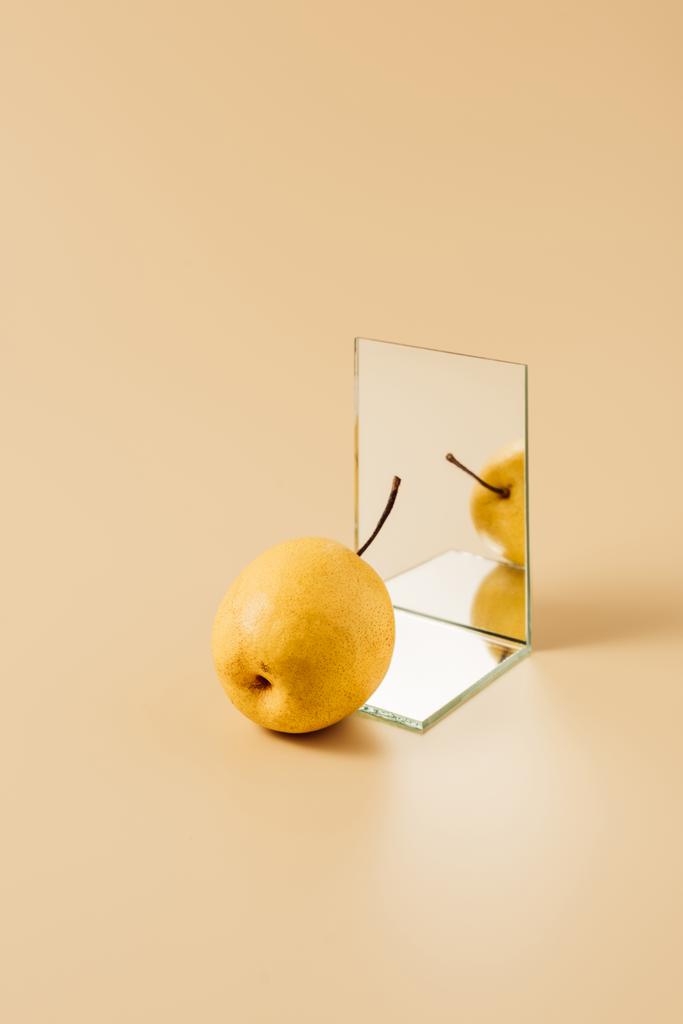 вкусная желтая груша, отражающаяся в двух зеркалах на бежевом столе
 - Фото, изображение