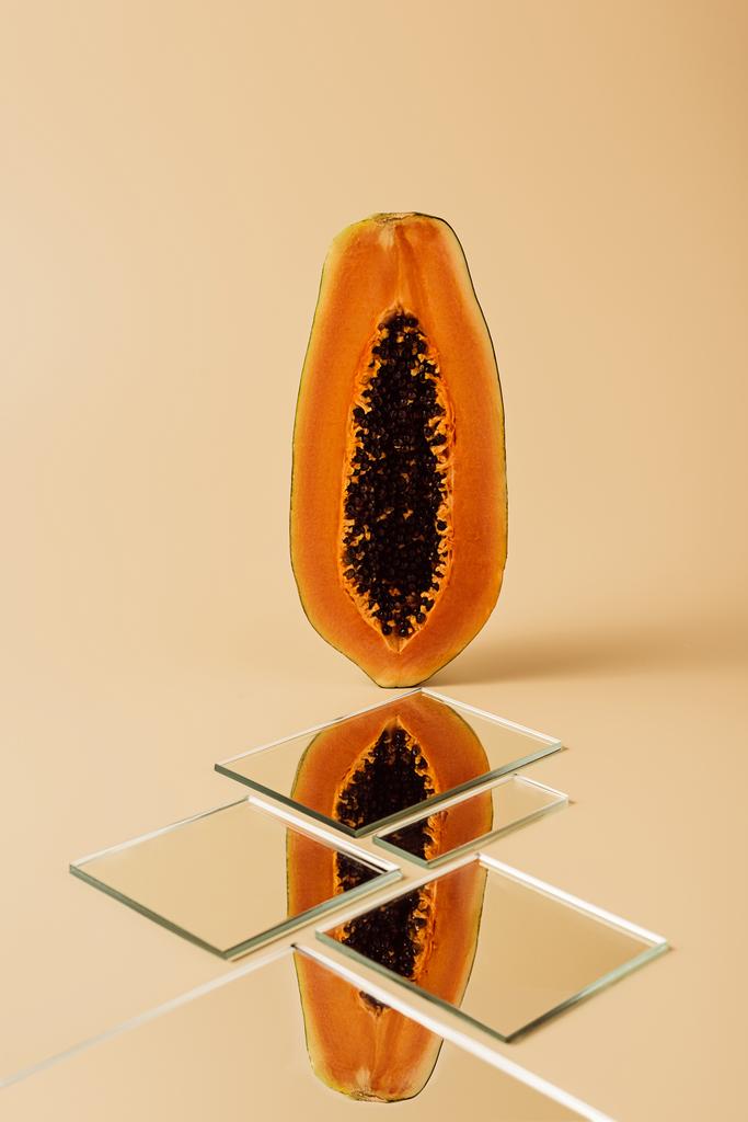 Hälfte der gelben Papaya spiegelt sich in Spiegeln auf beigem Tisch  - Foto, Bild