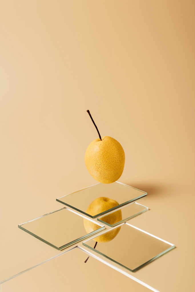 eine gelbe Birne spiegelt sich in Spiegeln auf beigem Tisch - Foto, Bild