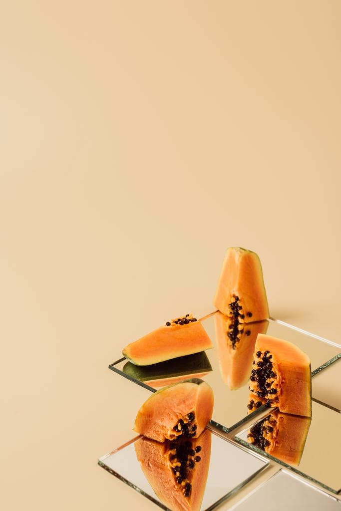 Papaya stukjes weerspiegelen in spiegels op beige tafel  - Foto, afbeelding