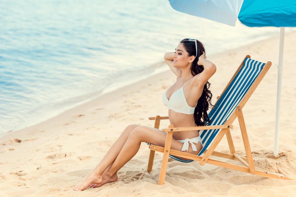 jolie fille assise sur une chaise de plage sous un parapluie près de la mer
 - Photo, image
