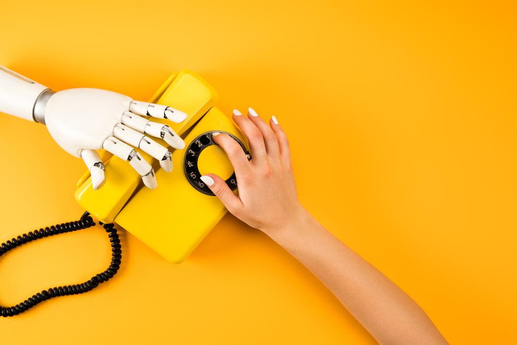 女性と黄色のヴィンテージの電話に手を伸ばしロボットのクロップ撮影 - 写真・画像