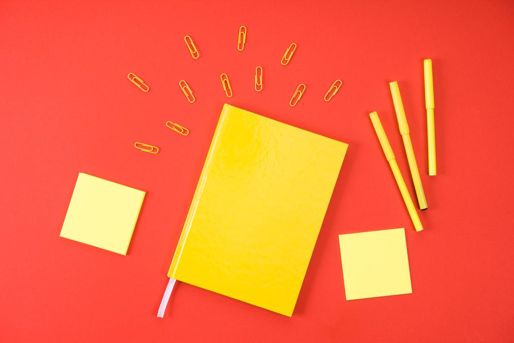 επίπεδη lay με κίτρινο σημειωματάριο με τις προμήθειες στο κόκκινο - Φωτογραφία, εικόνα