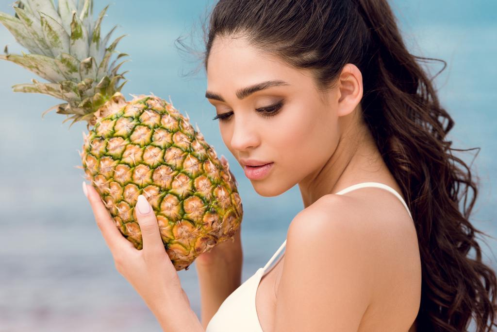Porträt eines schönen Mädchens im weißen Bikini mit süßer Ananas am Meer - Foto, Bild
