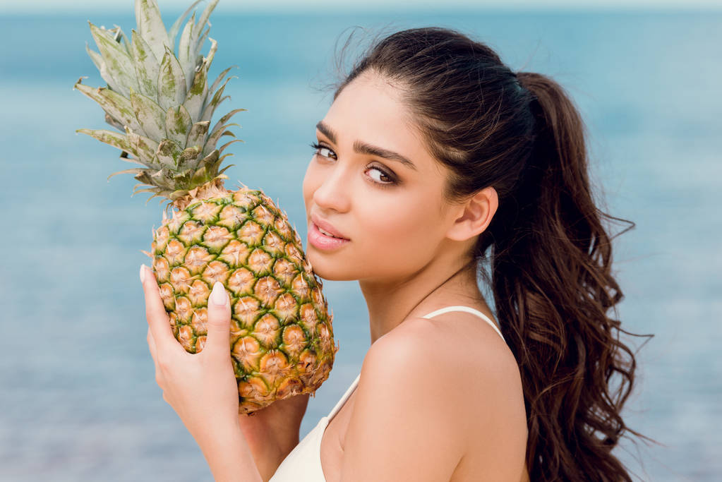портрет привлекательной молодой женщины, держащей сладкий ананас у моря
 - Фото, изображение