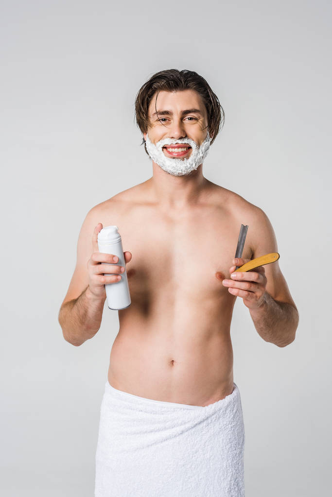 πορτρέτο της χαμογελαστός άνθρωπος στην λευκή πετσέτα με ξύρισμα αφρού στο πρόσωπο και το ίσιο ξυράφι στο χέρι απομονώνονται σε γκρι - Φωτογραφία, εικόνα