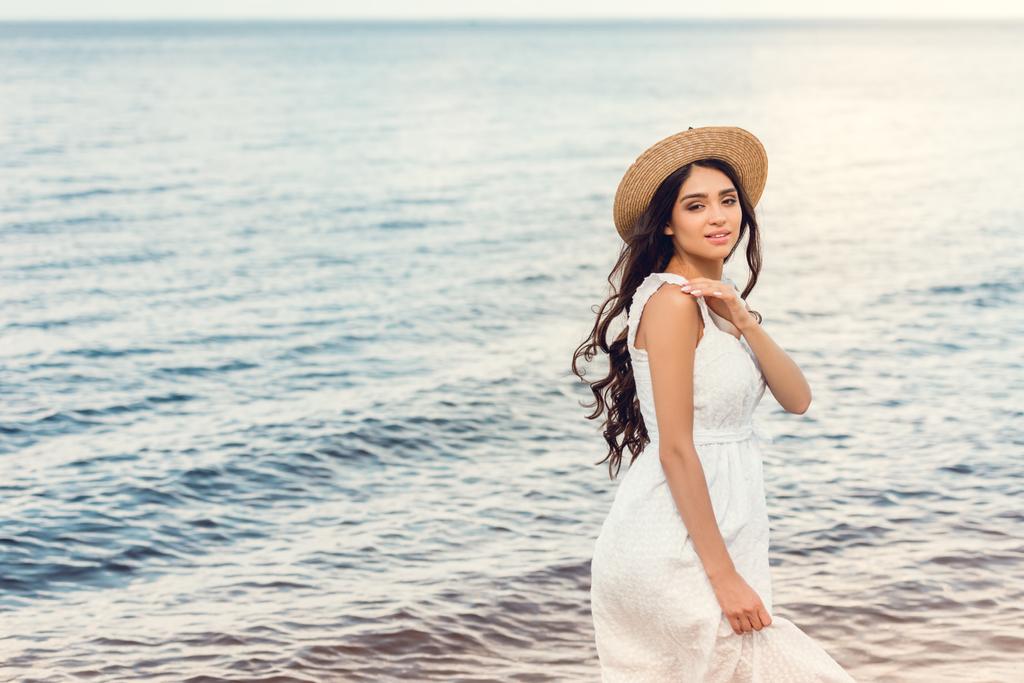 приваблива дівчина в солом'яному капелюсі, що йде біля моря влітку
 - Фото, зображення