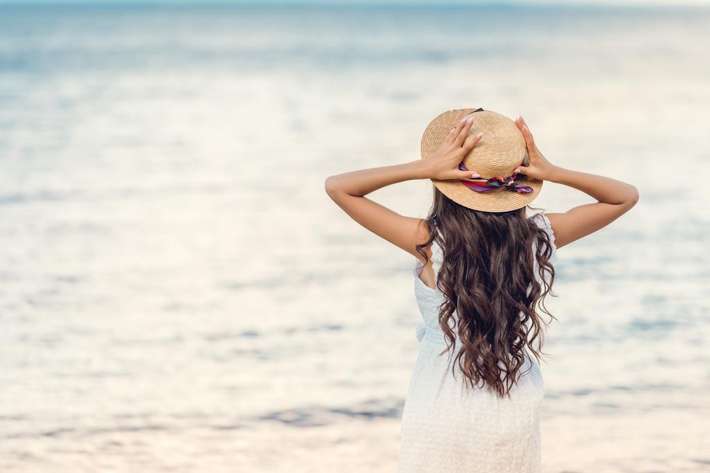 back view of girl in straw hat looking at sea - Photo, Image