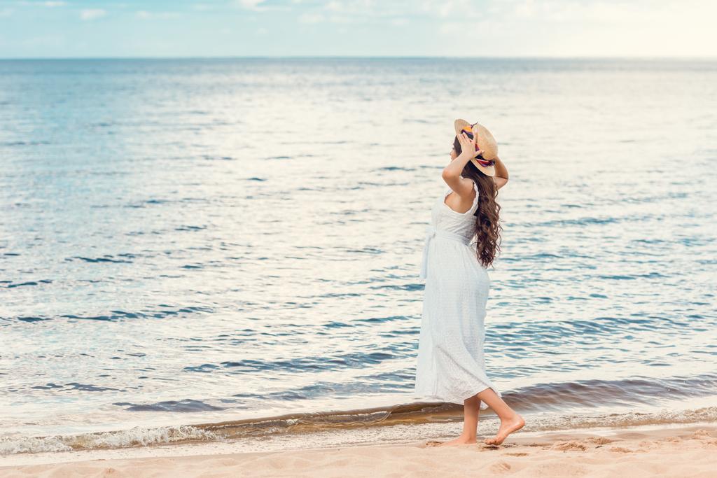 красивая девушка в белом платье прогуливается по песчаному пляжу у моря
 - Фото, изображение