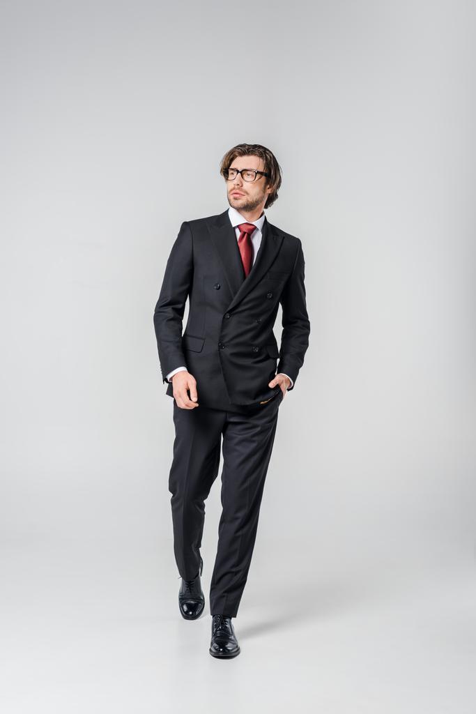 nuori liikemies tyylikäs puku ja silmälasit kävely harmaalla taustalla
 - Valokuva, kuva