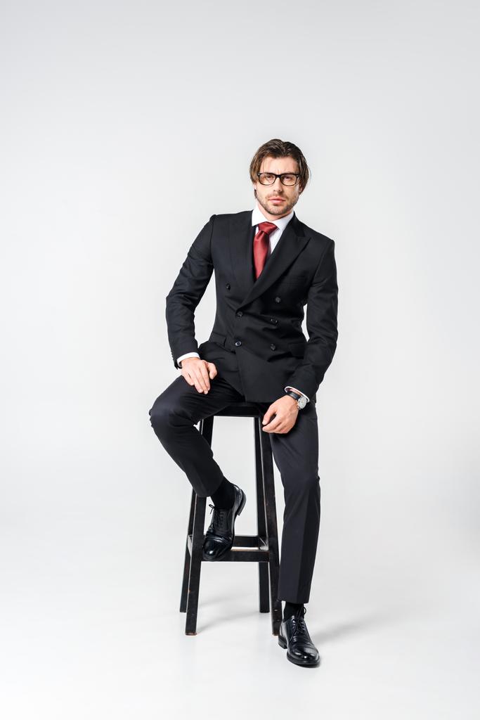スタイリッシュなスーツと灰色の背景に椅子に座っている眼鏡青年実業家 - 写真・画像
