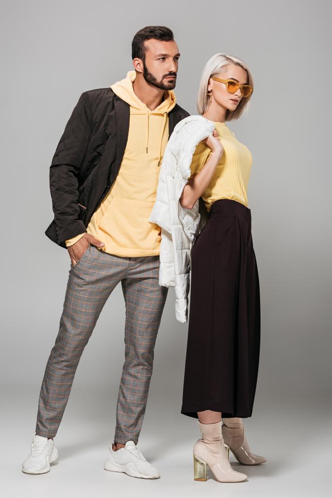 jonge stijlvolle paar poseren in herfst outfits op grijze achtergrond  - Foto, afbeelding